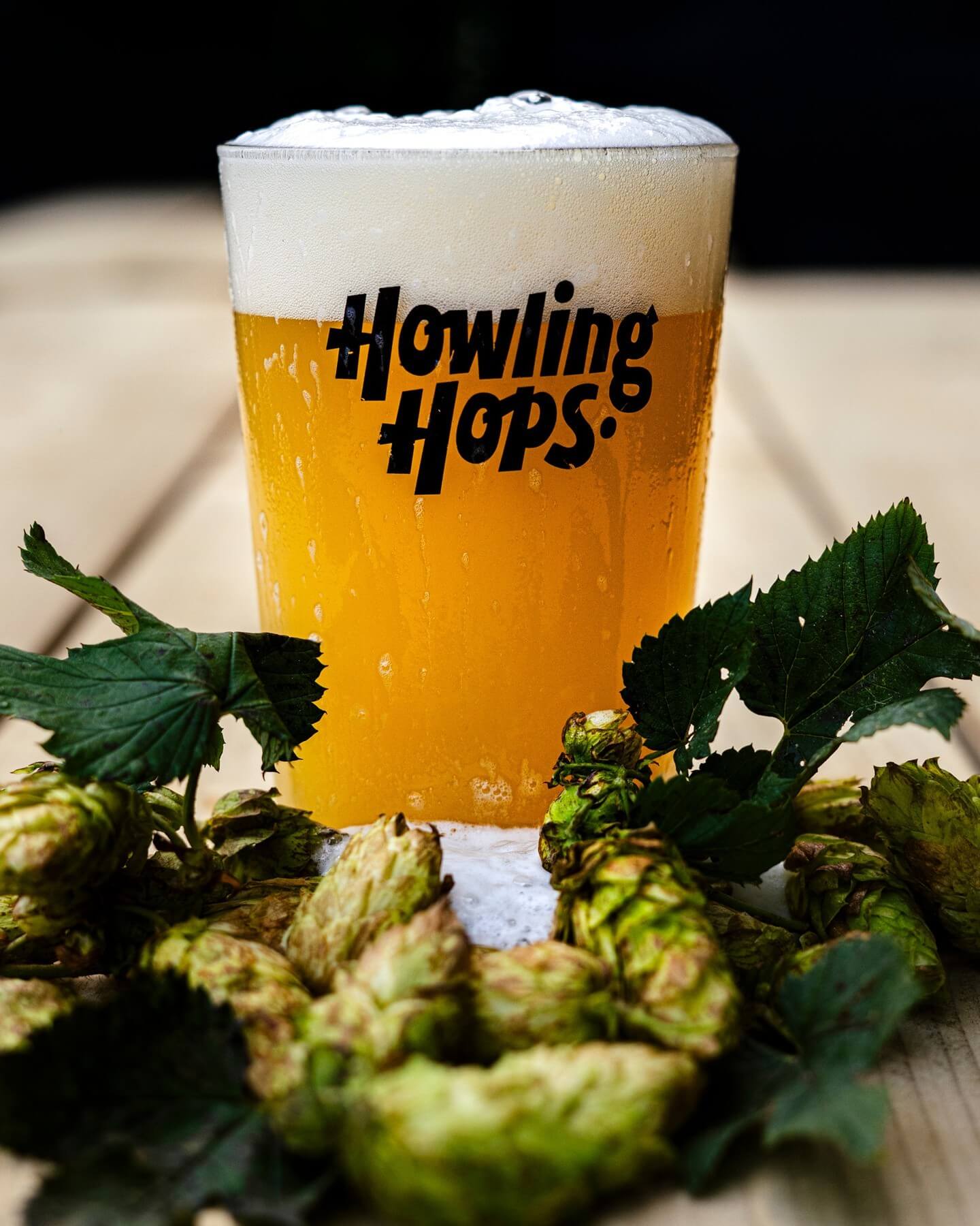 Howling Hops 'Fresh Hop Tropical Deluxe' 4.4% Pale Ale featuring fresh Ernest hops. A pint of the beer sits behind a pile of fresh Ernest hops on a table.