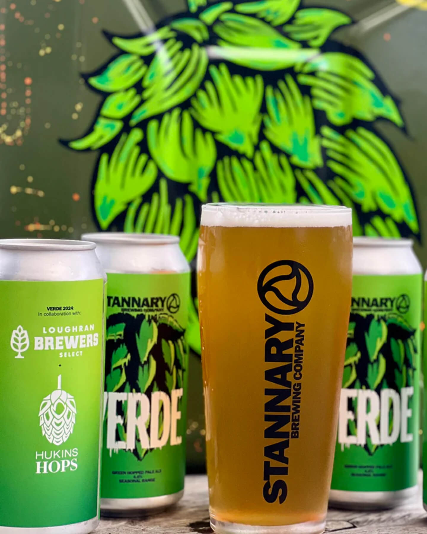 Stannary Brewing Company 'Verde' 4.6% Green Hop Pale featuring fresh Ernest hops. A pint of the beer sits in front of 3 cans & a hop cone drawing.