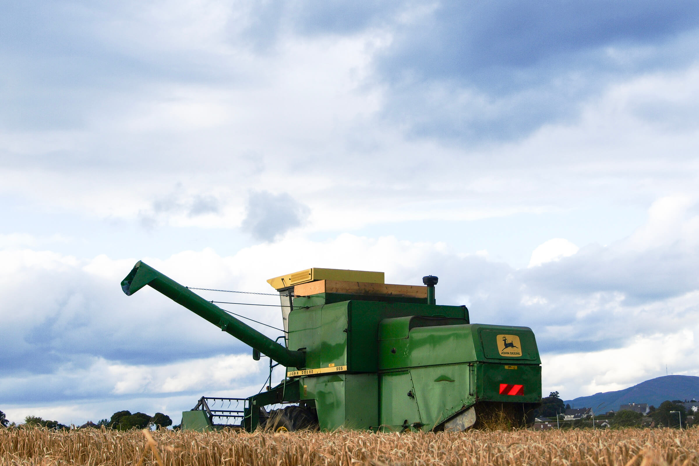 John Deer combine harvesting a field of spring barley malt on a cloudy spring day.